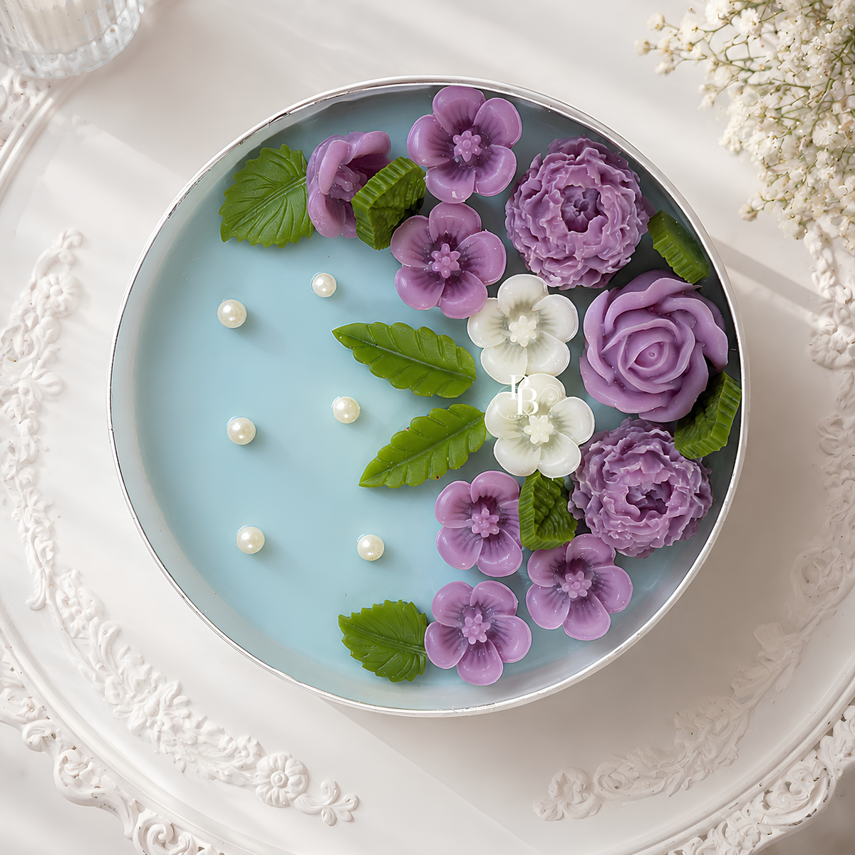 Scented candle in round blue wax with purple flowers, green leaves, and pearl-like dots