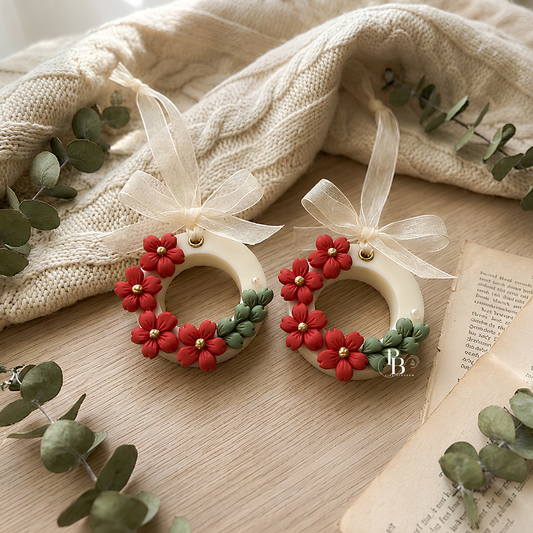 Handmade floral wax sachet wreath with red blossoms, green leaves, and cream ribbon bows