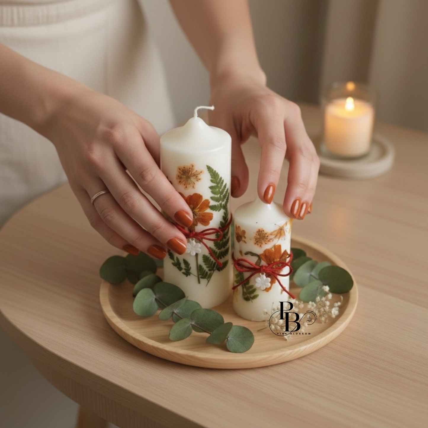 White pillar candle with dried flowers, red ribbon, on wooden tray with eucalyptus leaves