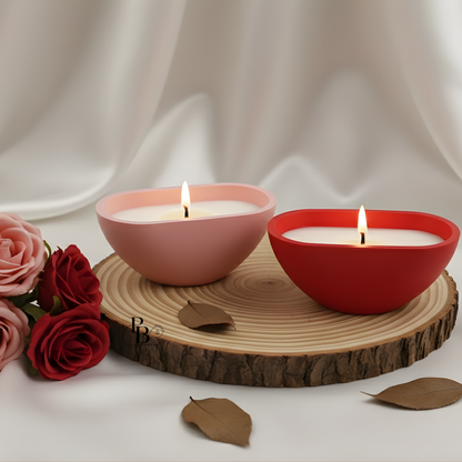 Two heart-shaped candle bowls, one pink and one red, on a wooden slice.