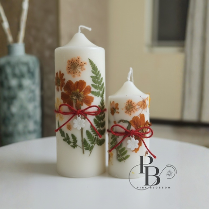 White pillar candles with dried botanical flowers and red ribbon, two-piece set