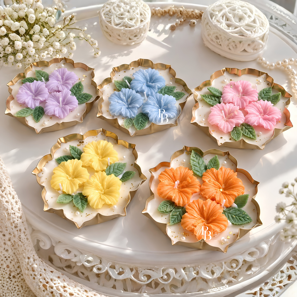 Floral hibiscus candles in pastel colors, gold scalloped holders on a tray