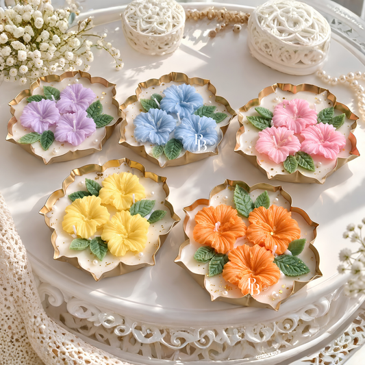 Floral hibiscus candles in pastel colors, gold scalloped holders on a tray