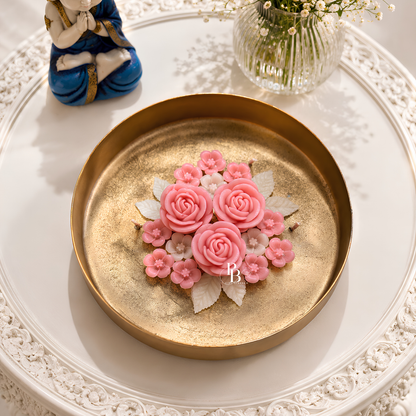 Gold-toned candle dish with pink rose floral topper on a decorative plate