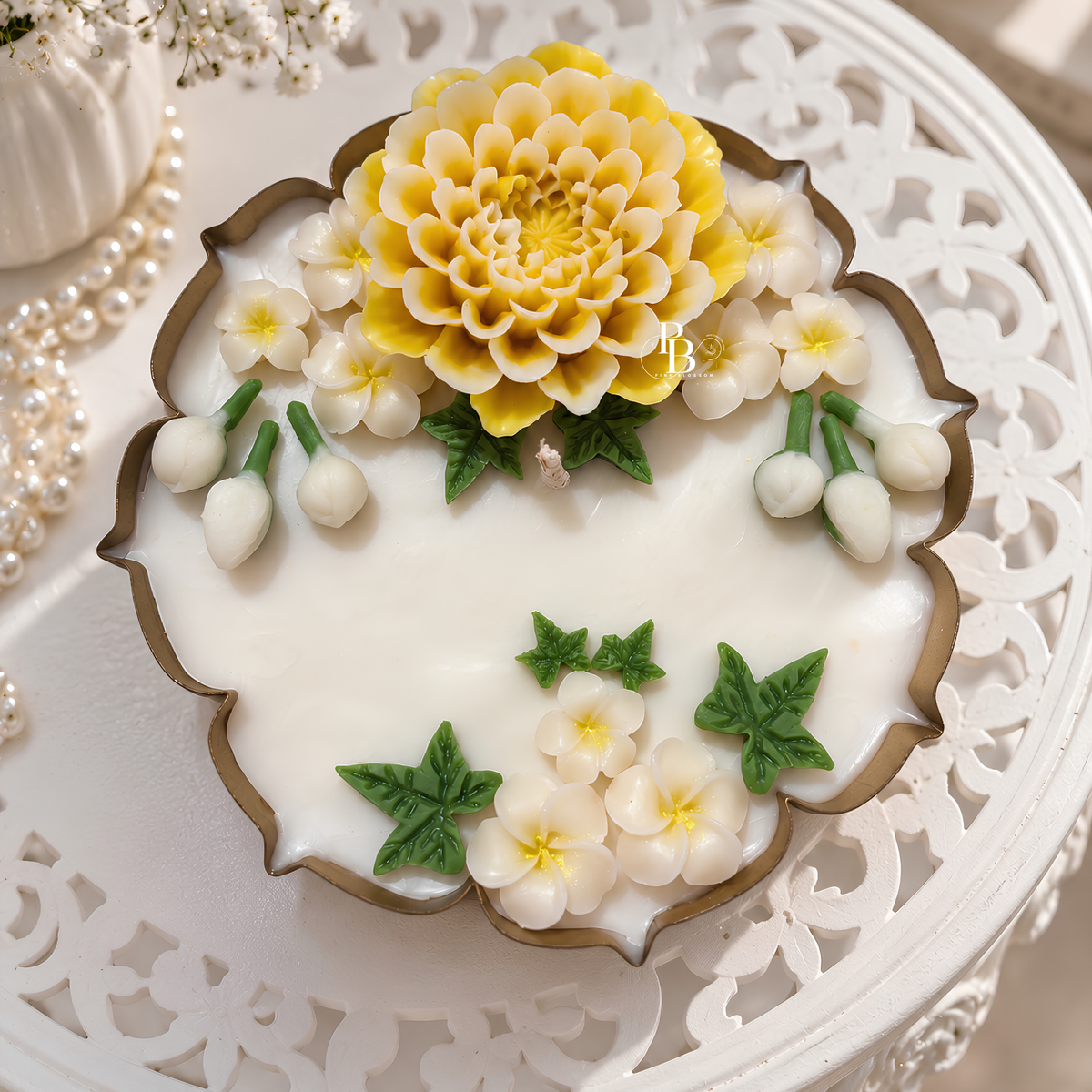 Floral wax candle with yellow and white blooms, green leaves, on a decorative base