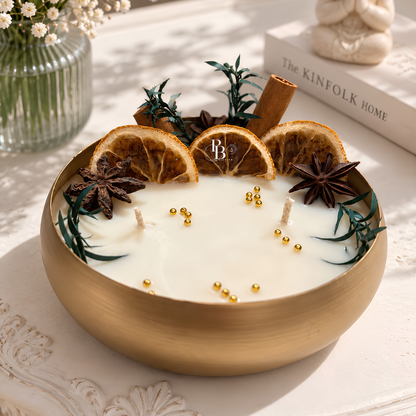 Round candle with white wax, orange slices, star anise, and cinnamon stick in gold container